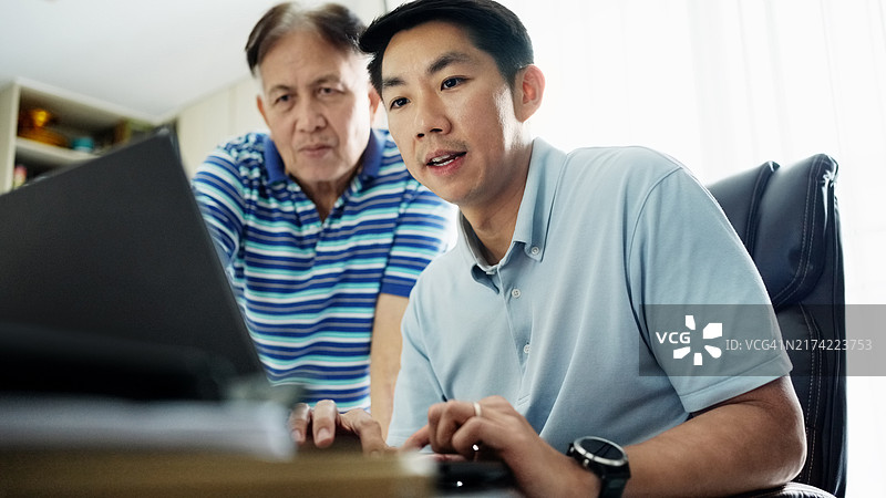 年长的男人站在家中使用笔记本电脑的儿子旁边图片素材