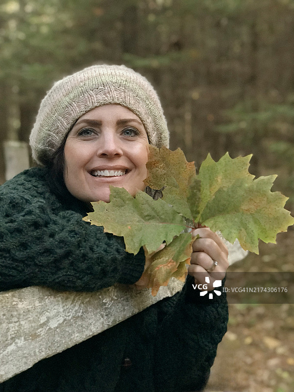 戴着针织贝雷帽和毛衣，手拿秋叶的女人图片素材