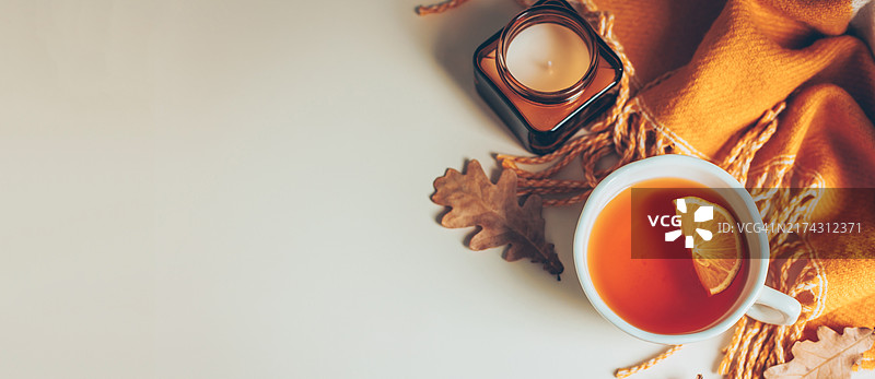 温暖的秋季橙色围巾、柠檬茶杯、秋季橡树叶在浅色背景上。顶视图，平铺，复制空间。北欧舒适风格概念。设计横幅。图片素材