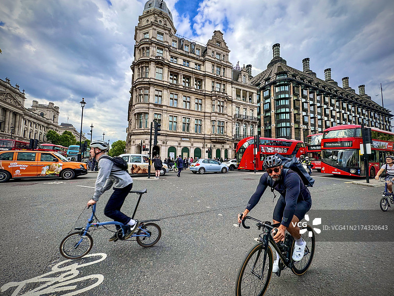 人们骑着自行车穿过伦敦繁忙的十字路口，周围满是汽车和公交车。图片素材