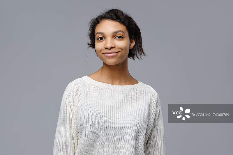 灰色背景上穿白色针织毛衣的乐观非洲女人特写图片素材
