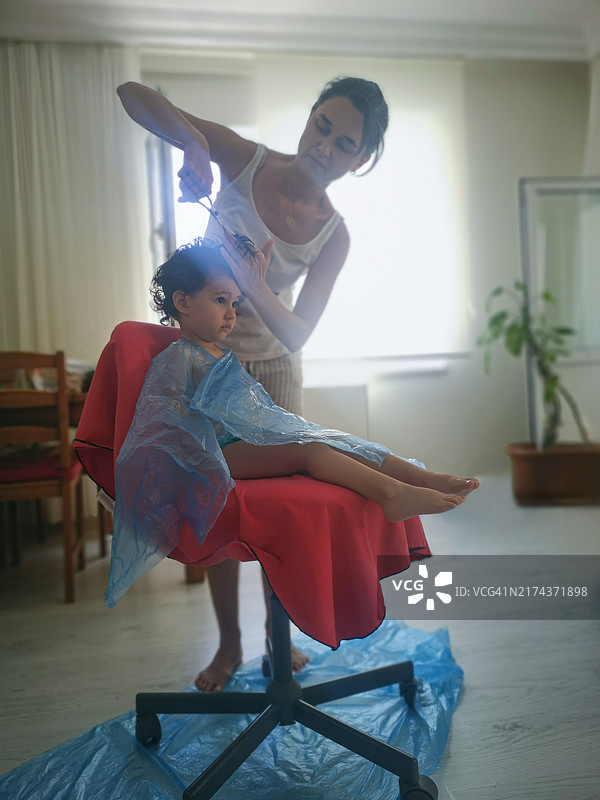 母亲在家为孩子理发，用塑料布遮盖图片素材