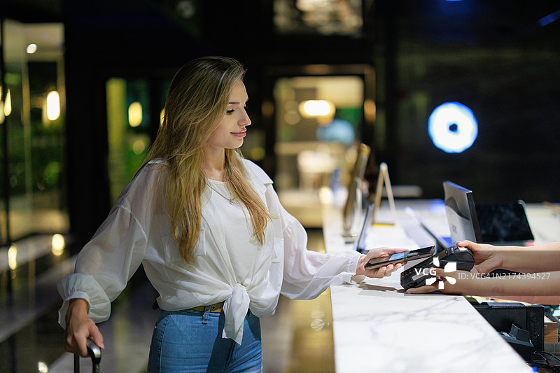 酒店接待服务,白人女性旅客在前台办理入住手续,行李在旁;旅行与旅游;商务出差;酒店员工与客人互动;奢华酒店夜晚的欢迎氛围。图片素材