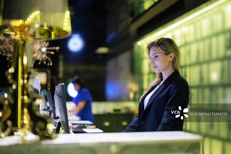 白人女性酒店经理在现代大堂前台工作，在电脑上处理酒店管理任务，在繁忙的工作环境中展示专业的酒店服务图片素材
