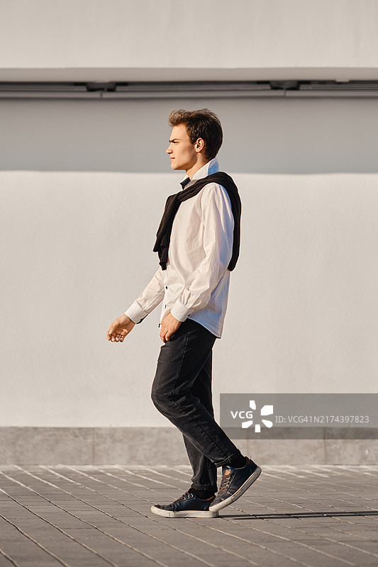 身穿白衬衫和毛衣的年轻男子走在街上图片素材