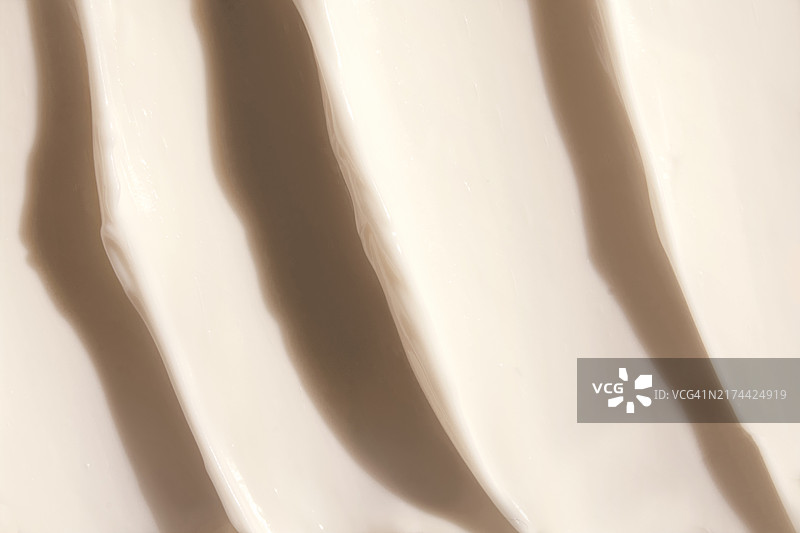 阳光下米色保湿霜的柔滑奶油质地，带有微妙的波浪。美容，化妆品纹理背景图片素材