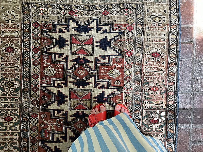 俯视站在古董波斯地毯上的红凉鞋女人的脚图片素材