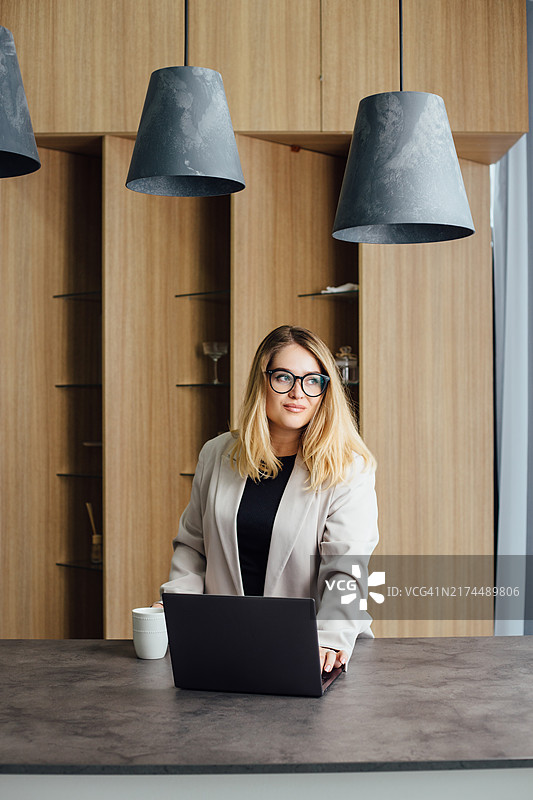 办公室厨房里用笔记本电脑的美丽女人图片素材