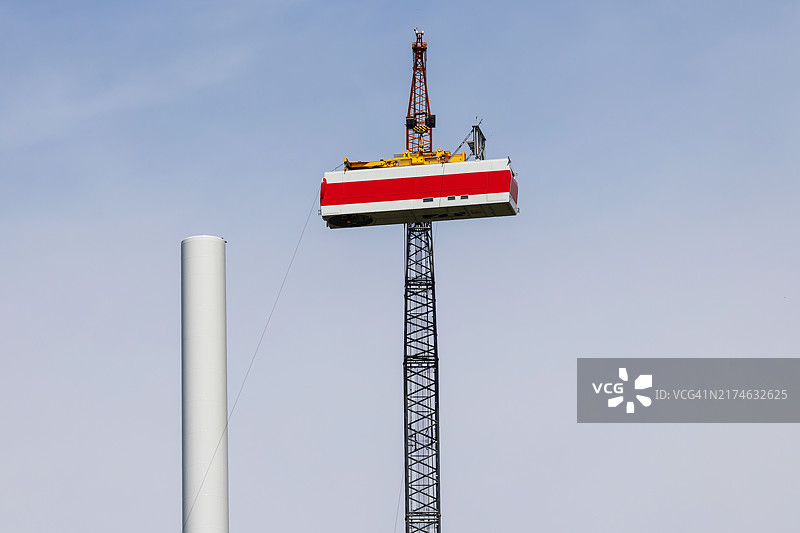风力涡轮机施工现场：大型起重机将涡轮机箱吊到塔上图片素材