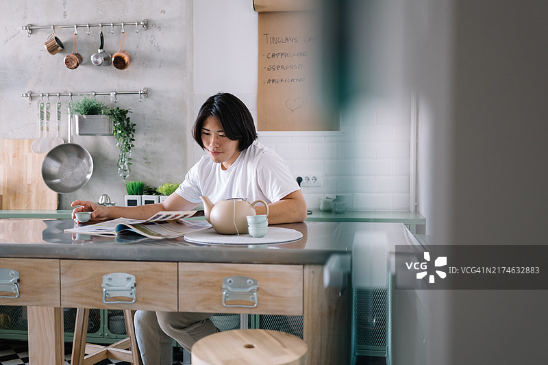 年轻亚洲男人在厨房阅读杂志图片素材