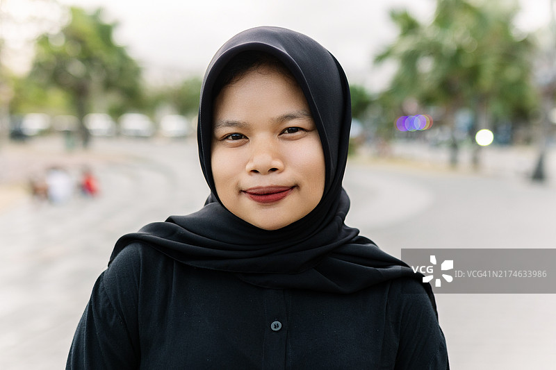 戴着头巾的年轻亚洲穆斯林女孩站在城市街道上看镜头图片素材