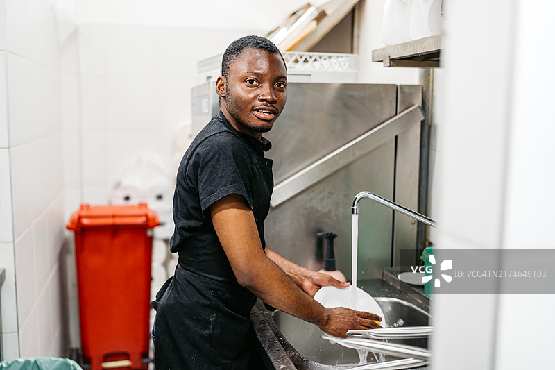 在商业厨房洗碗的年轻黑人男子图片素材