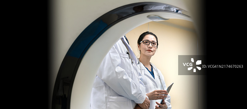 两位亚洲资深医生在CT扫描室使用平板电脑查看患者报告图片素材
