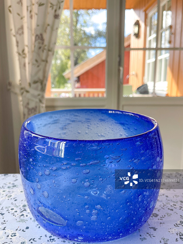 厚重蓝色玻璃碗置于花纹桌布，窗外红黄建筑图片素材