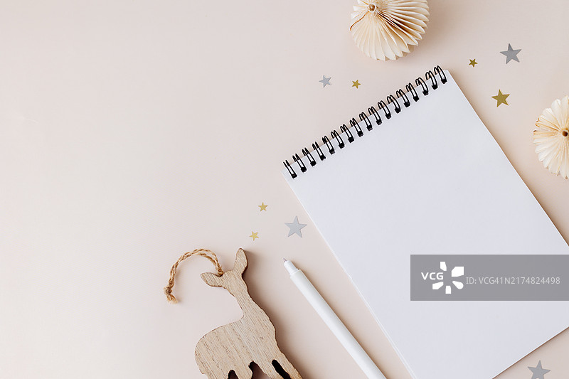 米色桌子背景上的空白笔记本、钢笔和圣诞装饰品。圣诞节、新年快乐、决心、目标、待办事项清单、策略和计划概念。带有复制空间的平面图图片素材