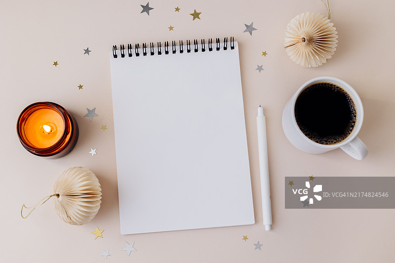 米色桌子背景上的空白笔记本、钢笔、杯中的黑咖啡、燃烧的蜡烛、圣诞装饰品。圣诞节，新年快乐，决心，目标，待办事项清单，策略和计划概念。具有复制空间的平面图图片素材