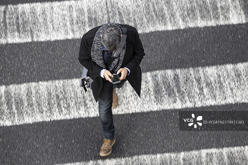 穿着冬装的白人男子在人行横道上行走并用智能手机聊天（俯视角度）图片素材
