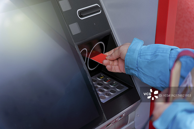 身穿蓝色夹克的女子将信用卡插入ATM取款机图片素材