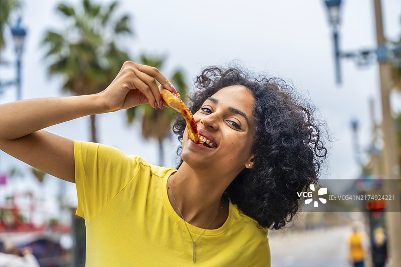 在街上享用外卖披萨的卷发拉丁裔女人图片素材