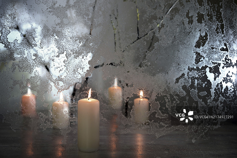 冬季圣诞新年装饰：温暖灯光和冰冻玻璃上的五支蜡烛图片素材