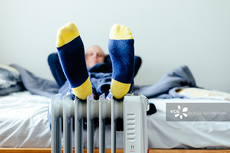 男人在家用电暖器上暖脚图片素材