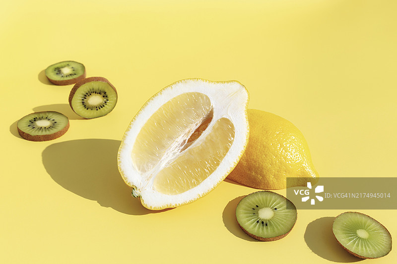 黄色背景上的半个柠檬与阴影，切片猕猴桃。健康饮食、旅行或度假概念图片素材