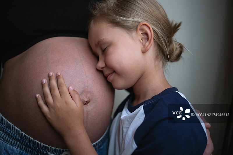 可爱女儿在家拥抱怀孕的母亲图片素材
