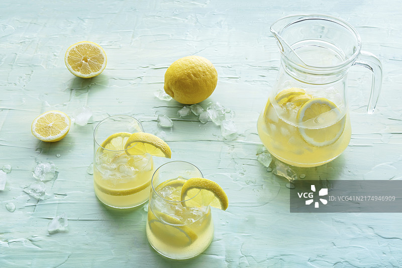 柠檬特调饮品。加冰柠檬水。蓝色背景上的两个玻璃杯和一个水罐。排毒饮料。新鲜自制鸡尾酒，美食摄影图片素材