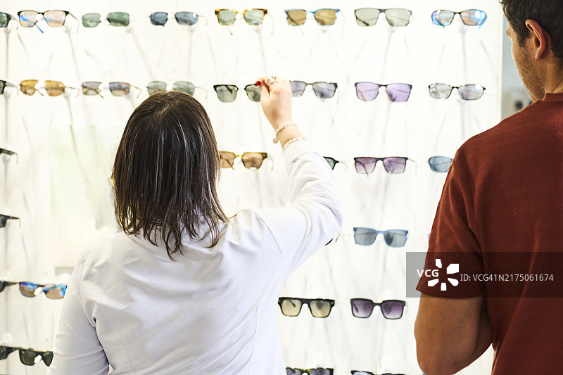 女验光师在货架上选择镜片，顾客在旁图片素材