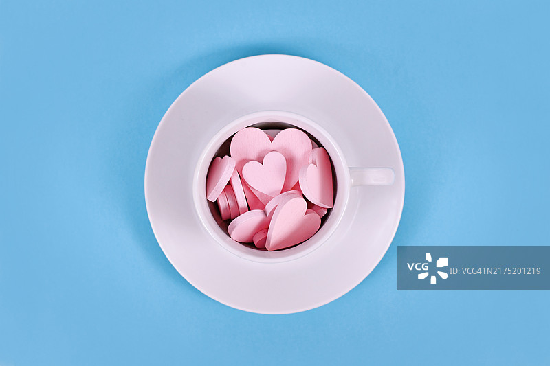 蓝色背景上白色茶杯中的粉色木制心形装饰品图片素材
