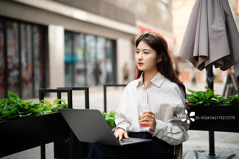 年轻漂亮的女人在城市街道的咖啡店里使用笔记本电脑图片素材
