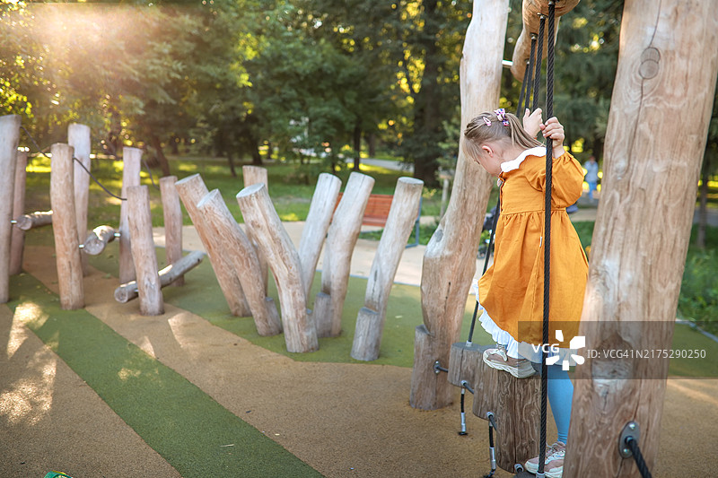 快乐时光：9岁唐氏综合征女孩在绿色公园的环保木制游乐场上玩耍，留白图片素材