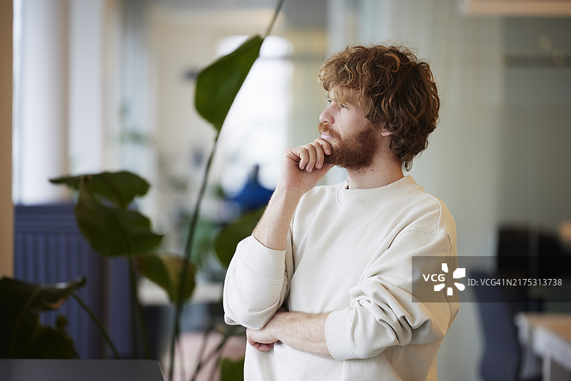 沉思的年轻商人站在办公室里图片素材