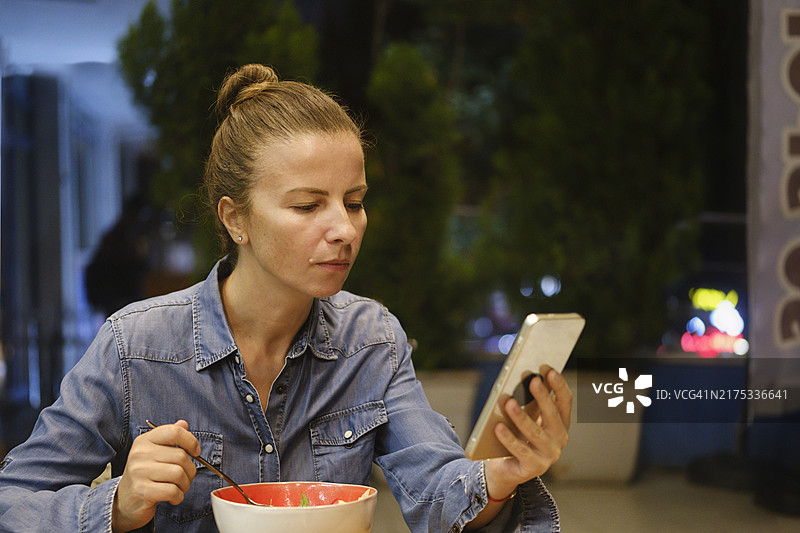 一位美丽的女性在户外用餐时专注地看着手机。图片素材
