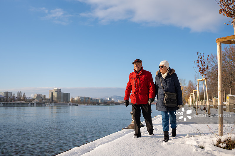 快乐的年长者在靠近河流和城市的雪地里享受冬季散步图片素材