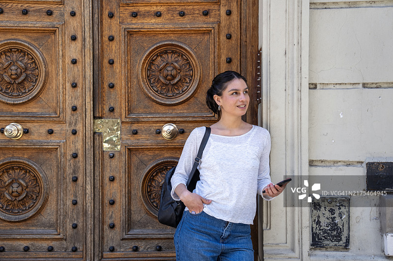 年轻女性倚靠在阿根廷布宜诺斯艾利斯圣特尔莫历史街区的一扇古董装饰门上图片素材