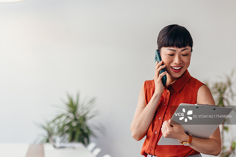 拿着写字板使用手机的自信的日本女商人图片素材