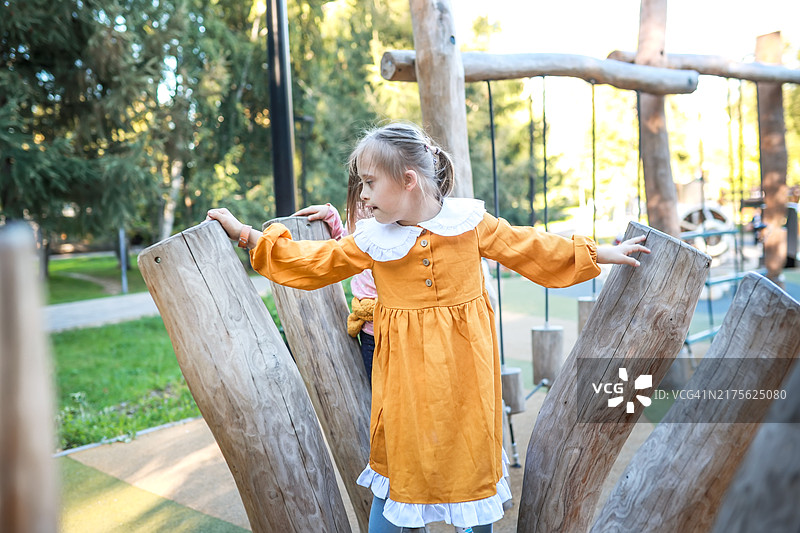在绿色公园的木制游乐场上玩耍的快乐的唐氏综合征9岁女童图片素材