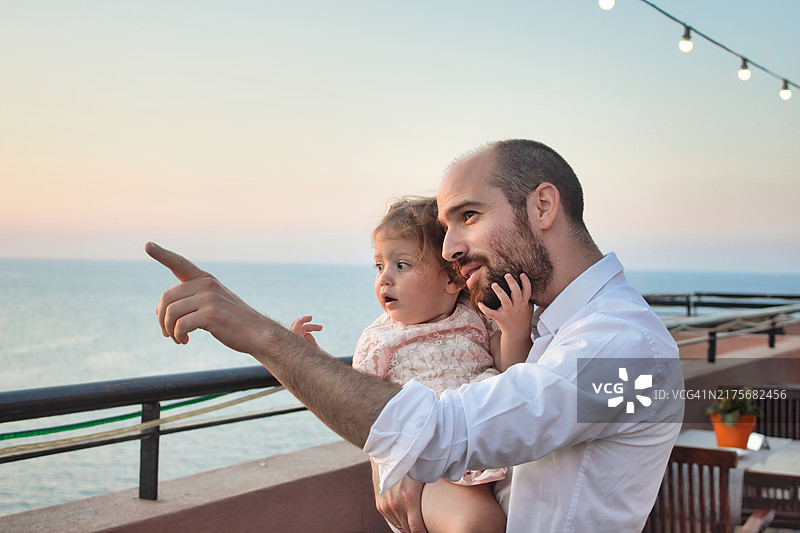 年轻的父亲抱着女儿在阳台上眺望图片素材