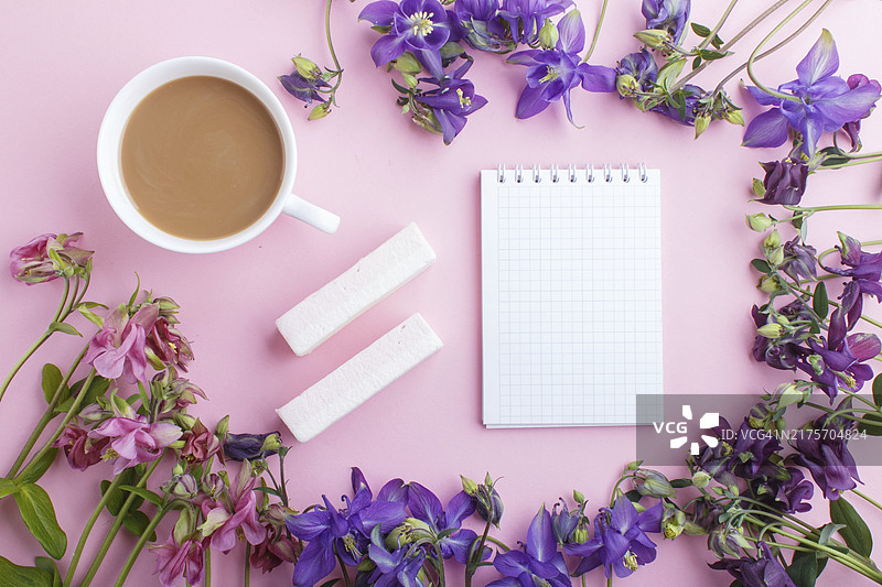 粉色和紫色耧斗菜花，以及粉色背景上的咖啡杯和笔记本。早晨，春天，时尚构图。平铺，顶视图，复制空间图片素材