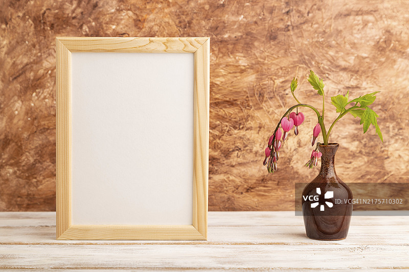 棕色混凝土背景陶瓷花瓶中粉色荷包牡丹木制画框，侧视图图片素材