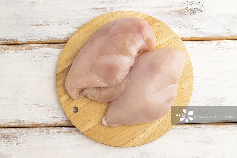 白色木质背景木制砧板上的香草调味生鸡胸肉。顶部视图，平铺，特写图片素材