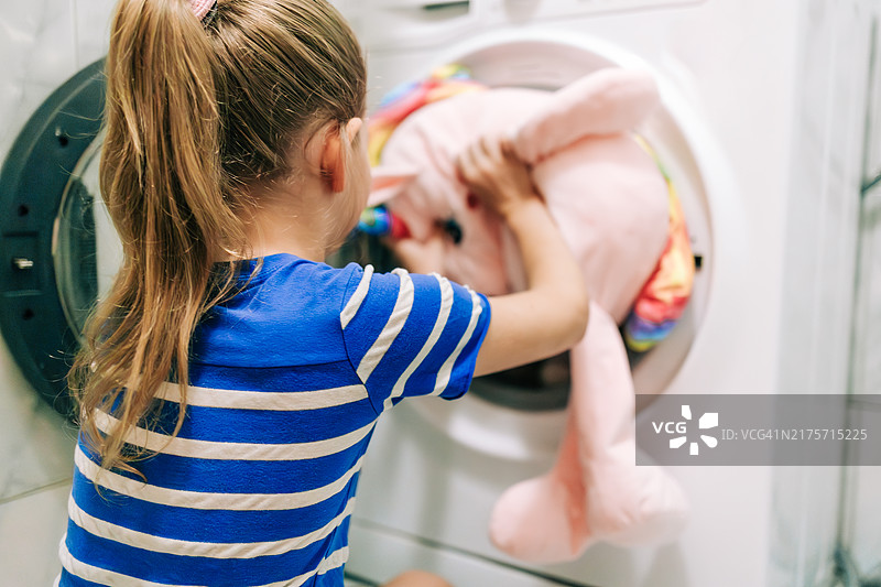 使用洗衣机清洗毛绒玩具的年轻小学生图片素材
