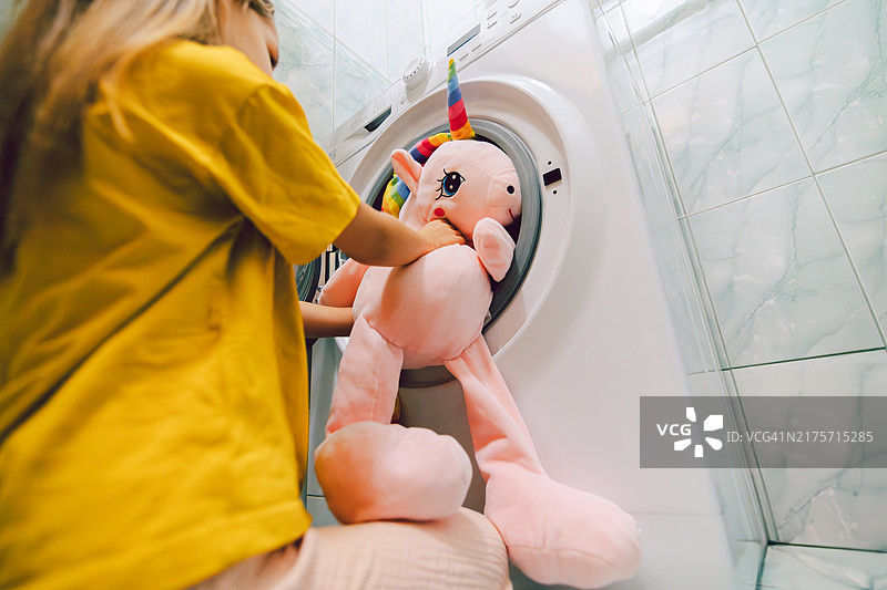 使用洗衣机清洗毛绒玩具的年轻小学生图片素材
