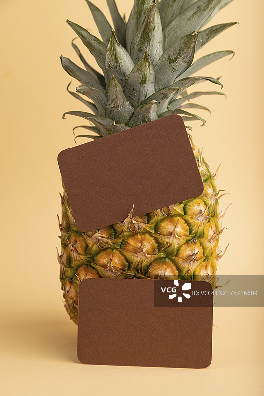 橙色背景上的棕色纸质名片与成熟的菠萝。侧视图，留白。热带、健康食品、度假、假日概念图片素材