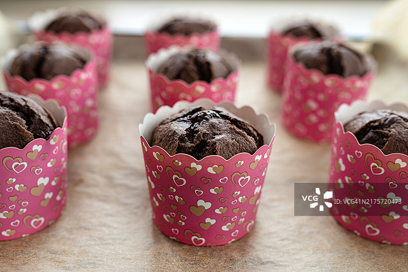 棕色巧克力松饼用白纸包裹，放在烤盘上的烘焙纸上。图片素材