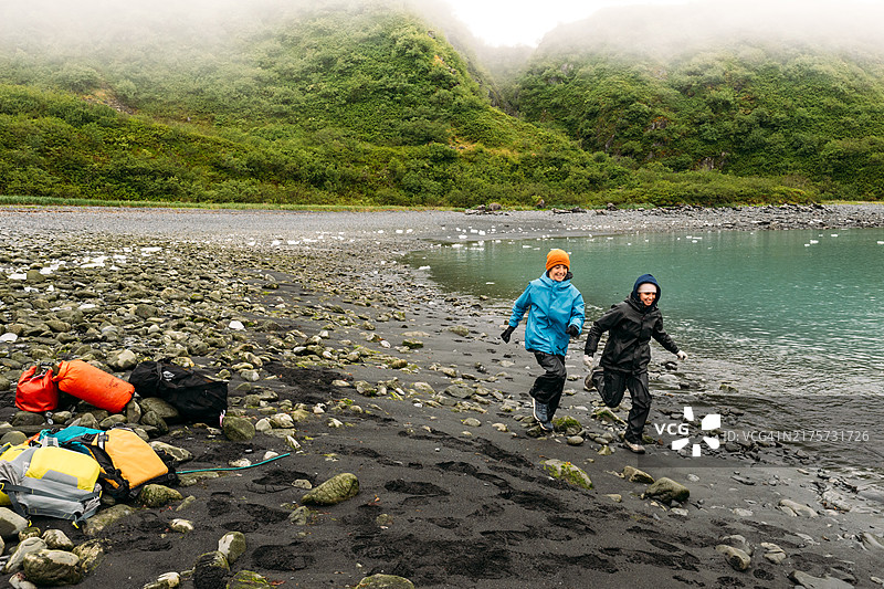 兄妹穿着雨衣在冰川海滩上奔跑图片素材