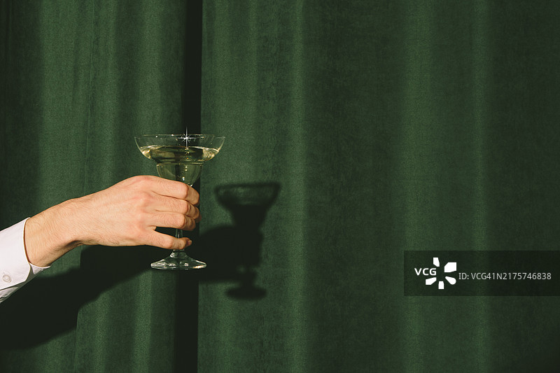 窗帘后伸出一只拿着马提尼酒杯的手图片素材