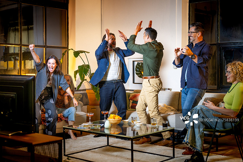 一群快乐的朋友在舒适的公寓里观看电视体育比赛图片素材