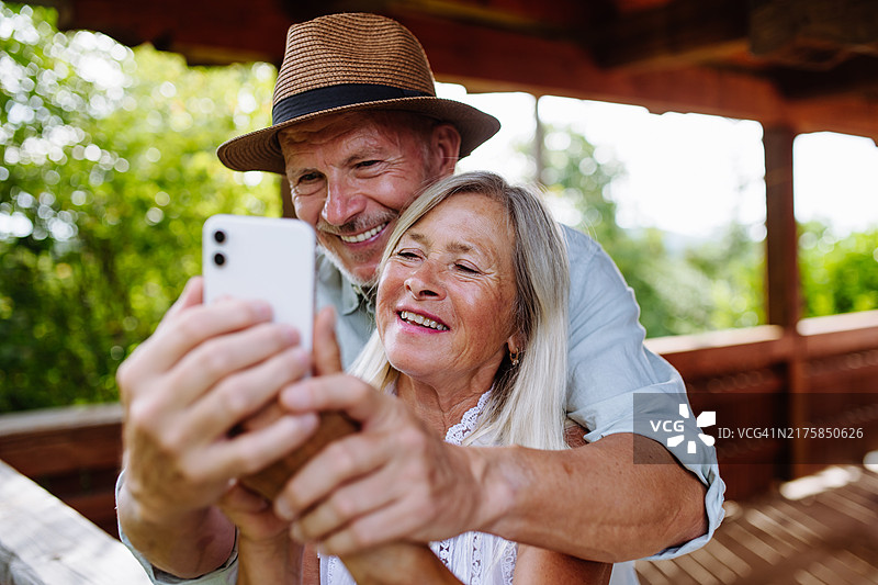 温馨时刻：年长的夫妇站在露台上拥抱，并用智能手机自拍图片素材